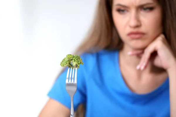 Blurred view of unhappy woman against light background, focus on fork with broccoli — Stock Photo, Image