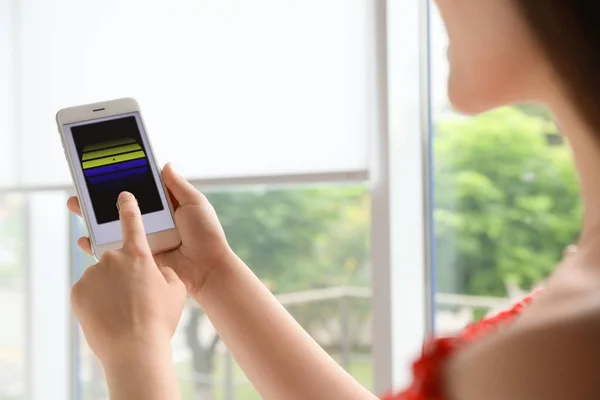 Woman using smart home application on phone to control window blinds indoors, closeup