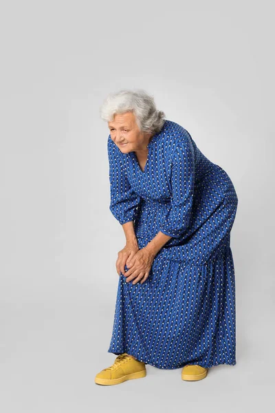 Ολόσωμο πορτρέτο της ανώτερης γυναίκας που έχει προβλήματα στο γόνατο σε γκρίζο φόντο — Φωτογραφία Αρχείου