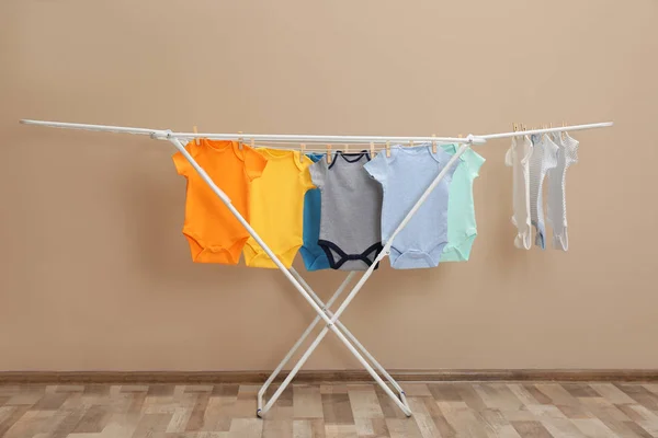 Verschillende schattige baby onesies opknoping op kledinglijn in de buurt van beige muur. Wasserij dag — Stockfoto