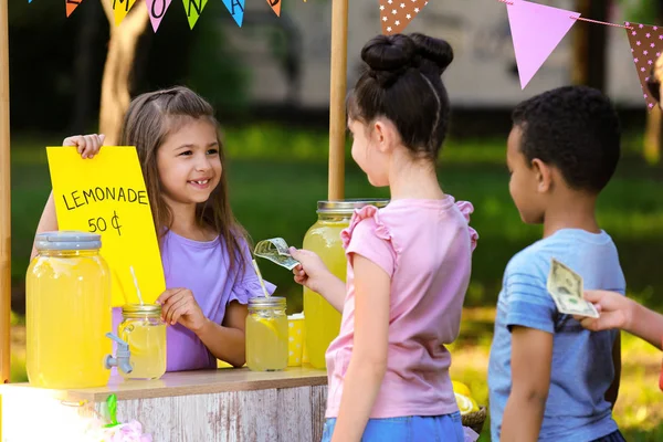 Little girl selling natural lemonade to kids in park. Summer refreshing drink — Stock Photo, Image