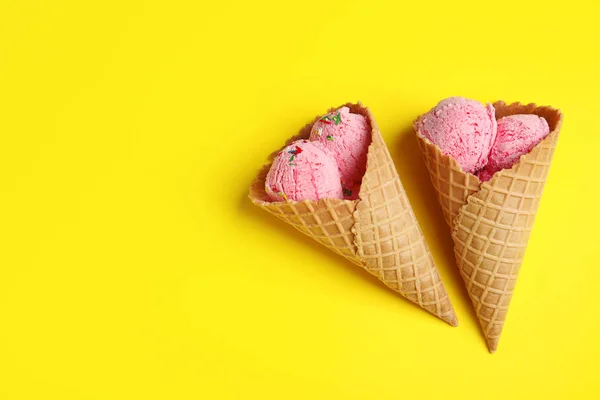 Delicioso helado en conos de oblea sobre fondo amarillo, tendido plano. Espacio para texto — Foto de Stock