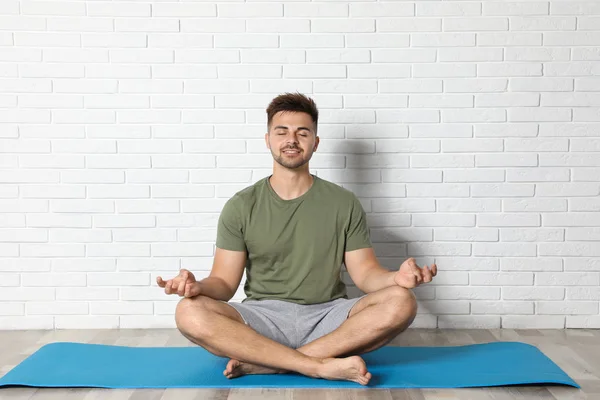 Hombre joven practicando yoga zen cerca de la pared de ladrillo blanco — Foto de Stock