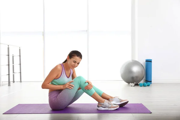 Jeune femme en tenue de sport ayant des problèmes de genou au gymnase. Espace pour le texte — Photo