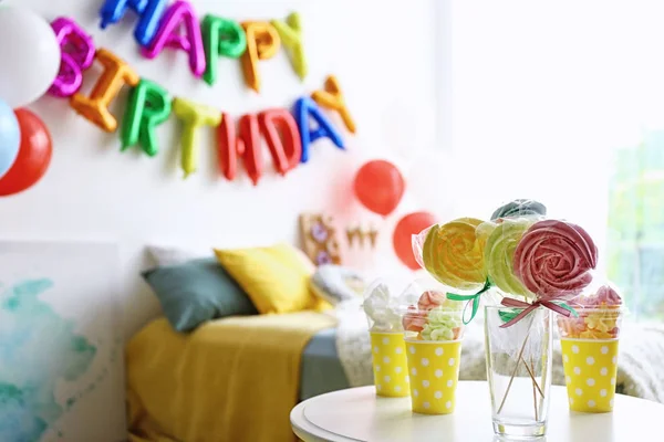 Table with treats and phrase HAPPY BIRTHDAY made of colorful balloon letters in modern bedroom. Space for text — Stock Photo, Image