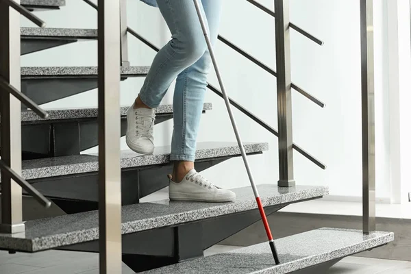 Blind person with long cane going down stairs indoors, closeup