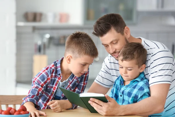 Pai e seus filhos lendo livro interessante na cozinha — Fotografia de Stock