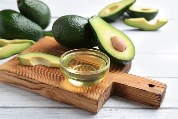 Доска с миской натурального масла и авокадо на белом деревянном фоне — стоковое фото