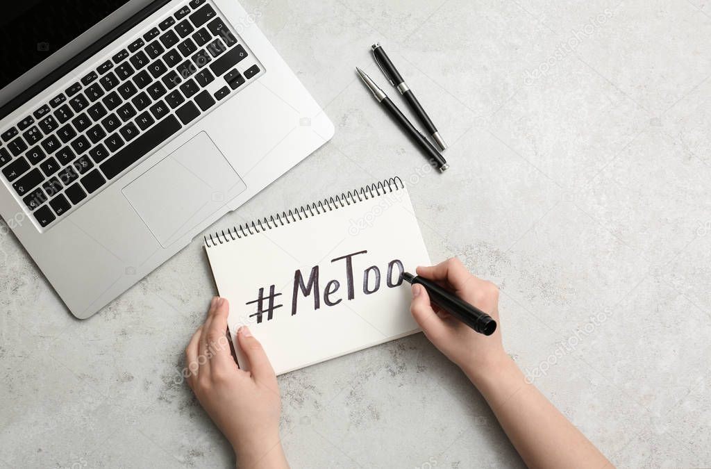 Woman writing hashtag METOO in notebook at grey table, top view. Stop sexual assault