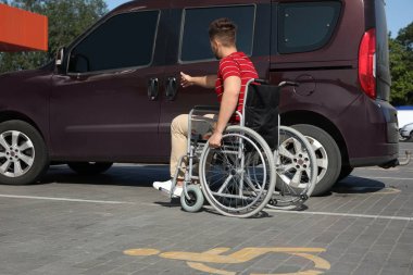Tekerlekli sandalyedeki genç adam otoparkta minibüsün kapısını açıyor