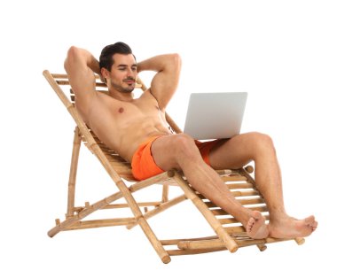 Beyaz arka plana karşı şezlonsun üzerinde laptop ile genç adam. Plaj aksesuarları