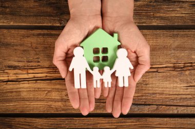 Ahşap arka plan üzerinde elinde aile ve yeşil ev figürleri tutan kadın, üst görünümü