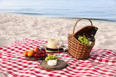 Güneşli plajda piknik sepeti ve ürünleri ile damalı battaniye