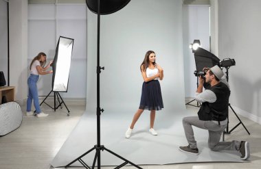 Asistan modern stüdyoda genç kadının fotoğrafını çeken profesyonel fotoğrafçı