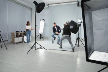 Asistan modern stüdyoda genç adamın fotoğrafını çeken profesyonel fotoğrafçı