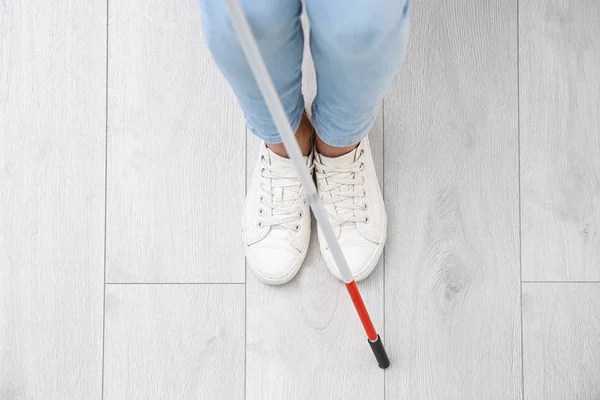 Blind person with long cane standing indoors, top view