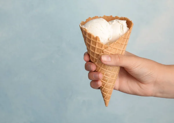 Mujer sosteniendo delicioso helado en cono de oblea sobre fondo azul claro, primer plano. Espacio para texto — Foto de Stock