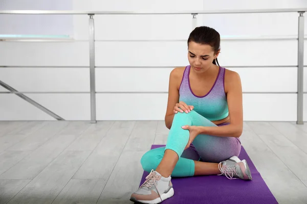 Mujer joven en ropa deportiva que tiene problemas de rodilla en el gimnasio. Espacio para texto —  Fotos de Stock