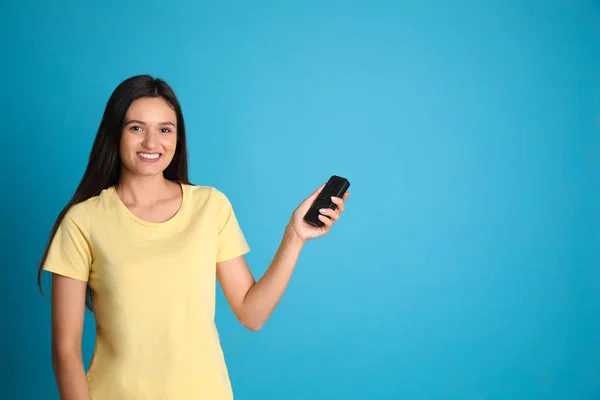 Feliz joven mujer que opera el aire acondicionado con control remoto sobre fondo azul claro. Espacio para texto — Foto de Stock