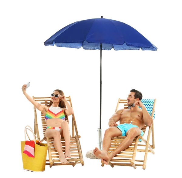 Giovane coppia scattare selfie su sedie a sdraio sotto l'ombrello sullo sfondo bianco. Accessori da spiaggia — Foto Stock