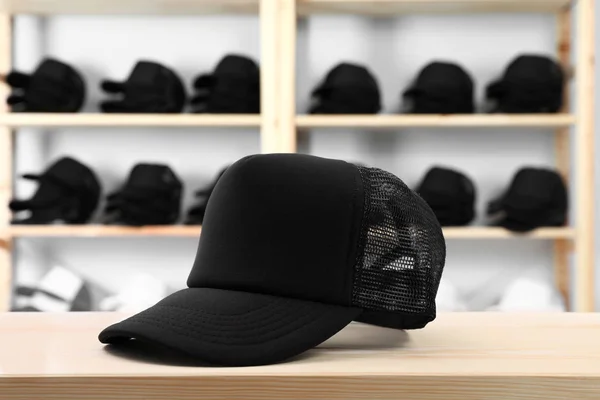 Gorra negra en blanco sobre mesa de madera en tienda. Prepárate para el diseño — Foto de Stock