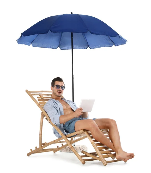 Young man with tablet on sun lounger under umbrella against white background. Beach accessories — Stock Photo, Image