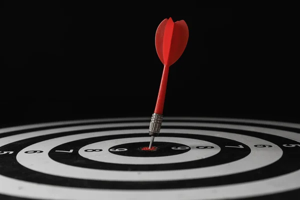 Red arrow hitting target on dart board against black background — Stock Photo, Image