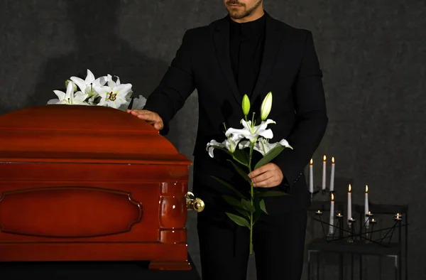 Young man with white lilies near casket in funeral home, closeup — Stock Photo, Image