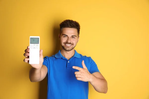 Jovem feliz com ar condicionado controle remoto no fundo amarelo — Fotografia de Stock