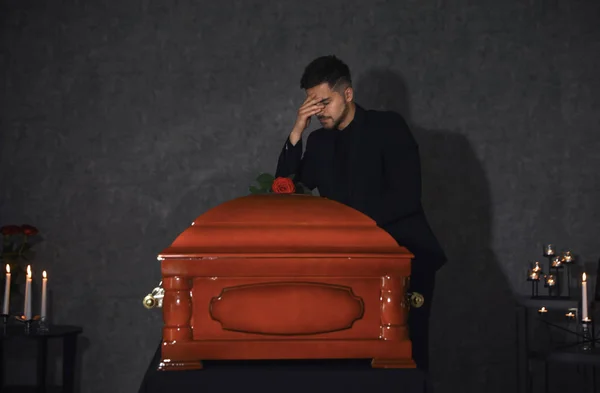 Sad young man near funeral casket with red rose in chapel — Stock Photo, Image