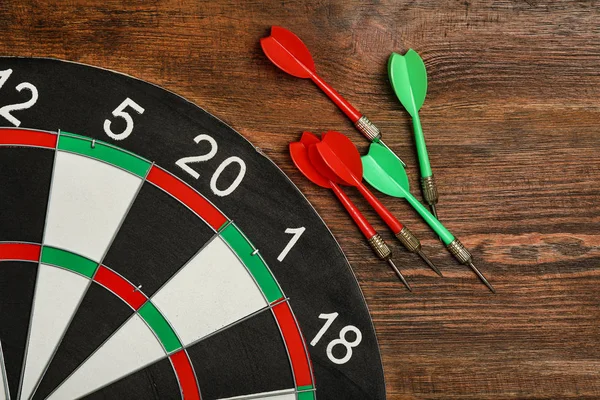 Dart board with color arrows on wooden background, top view — Stock Photo, Image