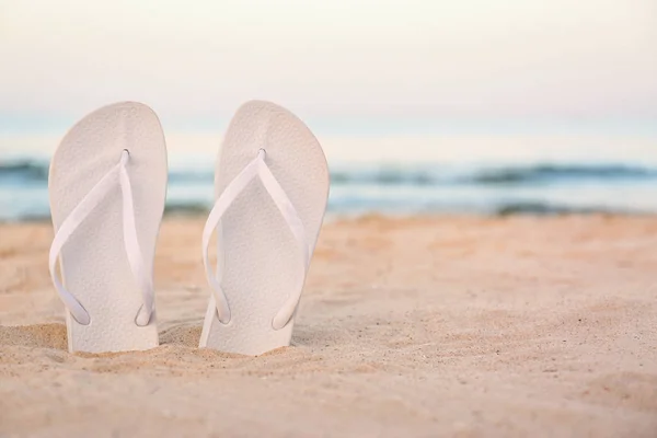 Infradito bianche sulla sabbia vicino al mare, spazio per il testo. Accessori da spiaggia — Foto Stock