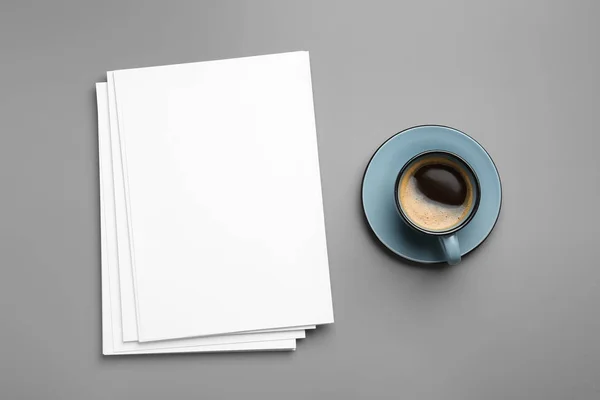 Leere Papierbögen für Broschüren und Kaffeebecher auf grauem Hintergrund, flach gelegt. Attrappe — Stockfoto
