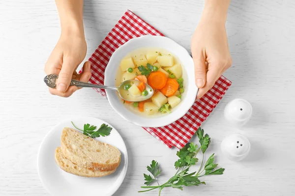 Женщина ест свежий овощной суп на белом деревянном столе, вид сверху — стоковое фото