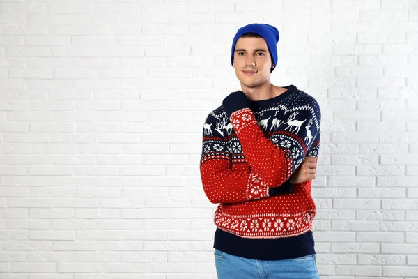 Portrait of young man in Christmas sweater and hat near white brick wall. Space for text — Stock Photo, Image