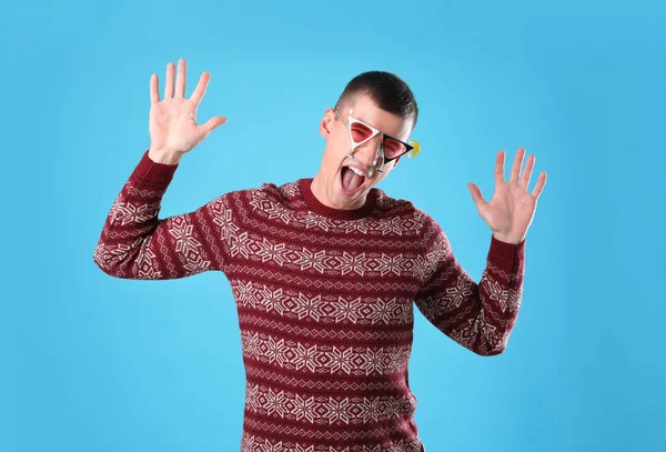 Jeune homme émotionnel en pull de Noël et lunettes de fête sur fond bleu clair — Photo