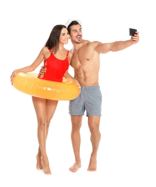 Giovane coppia attraente in beachwear con anello gonfiabile prendendo selfie su sfondo bianco — Foto Stock