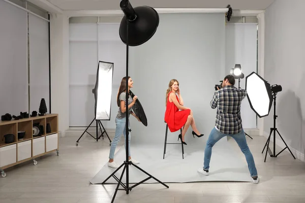 Fotógrafo profesional con asistente tomando fotos de una joven en un estudio moderno — Foto de Stock