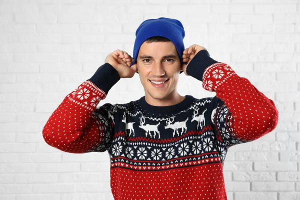 Portrait of young man in Christmas sweater and hat near white brick wall — Stock Photo, Image