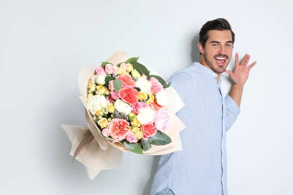 Jovem homem bonito com lindo buquê de flores no fundo claro — Fotografia de Stock