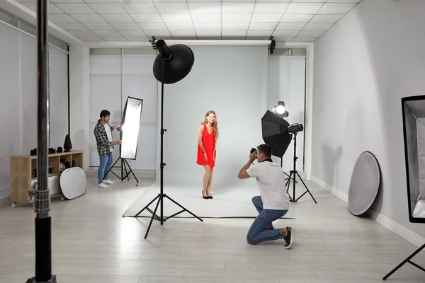Asistan modern stüdyoda genç kadının fotoğrafını çeken profesyonel fotoğrafçı — Stok fotoğraf