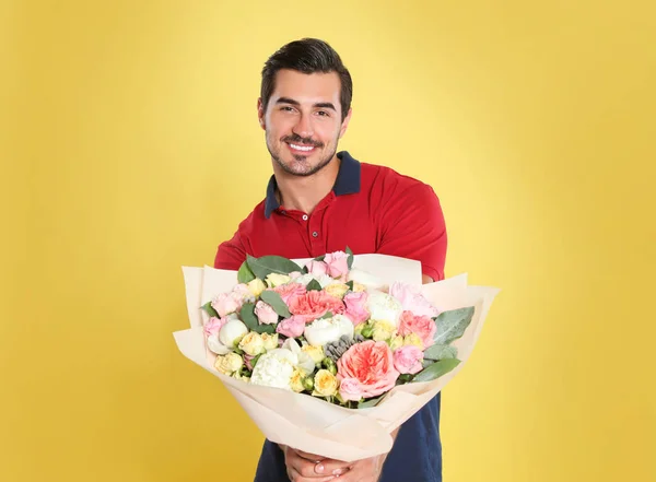 Jovem homem bonito com lindo buquê de flores no fundo amarelo — Fotografia de Stock