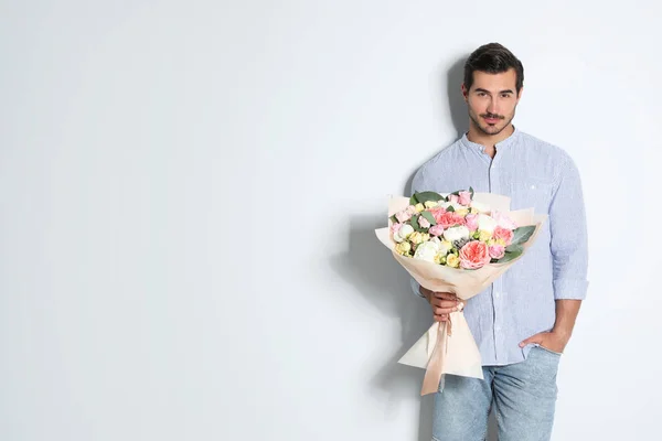Jovem homem bonito com lindo buquê de flores no fundo claro, espaço para texto — Fotografia de Stock