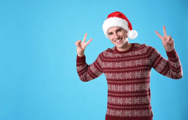 Portrait of young man in Christmas sweater and Santa hat on light blue background — Stock Photo, Image