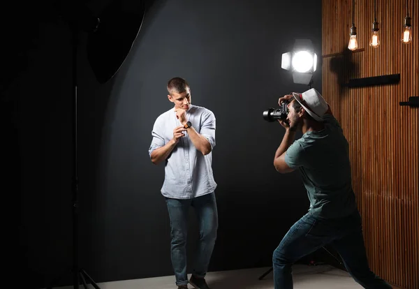 Fotógrafo profesional tomando fotos de un joven sobre fondo gris oscuro en un estudio moderno — Foto de Stock
