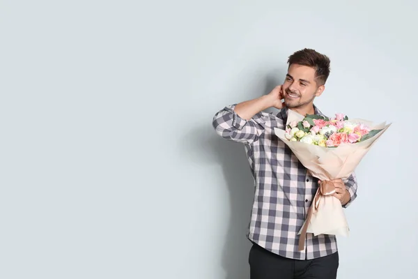 Young handsome man with beautiful flower bouquet on light background, space for text