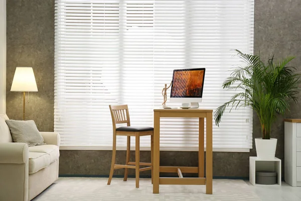Comfortable workplace near window with blinds in room — Stock Photo, Image