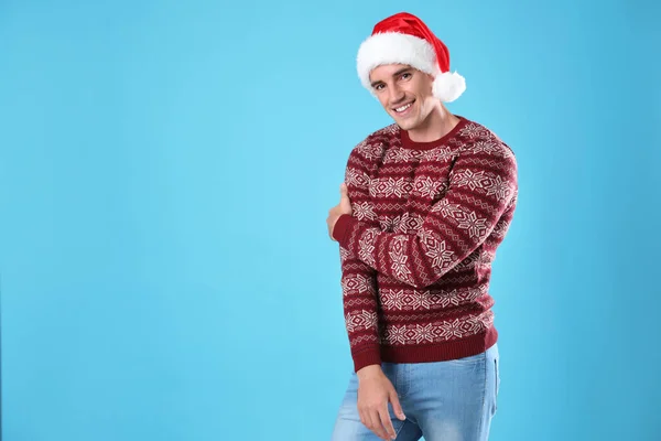 Portrait of young man in Christmas sweater and Santa hat on light blue background. Space for text — Stock Photo, Image