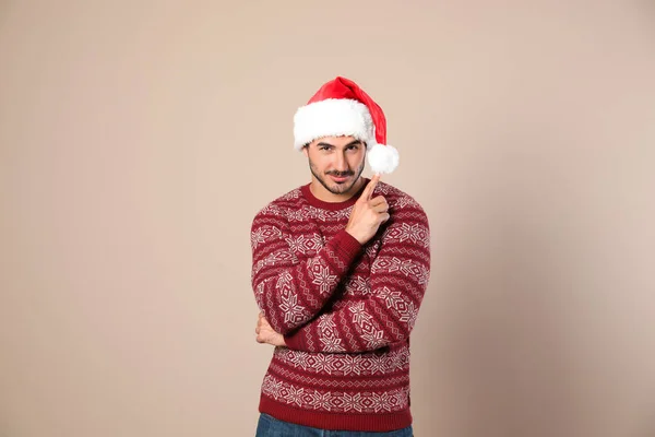 Portrait of young man in Christmas sweater and Santa hat on beige background — Stock Photo, Image