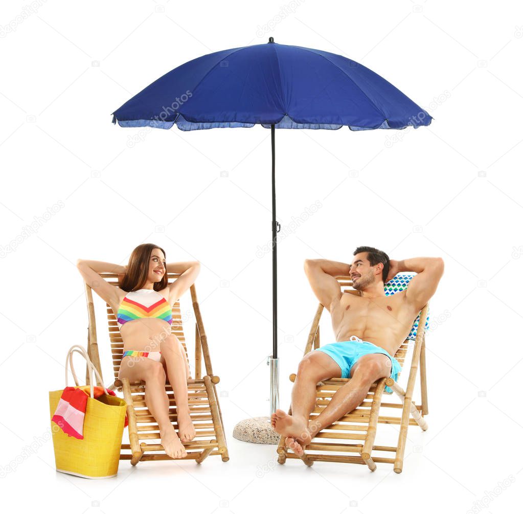 Young couple with beach accessories on sun loungers against white background